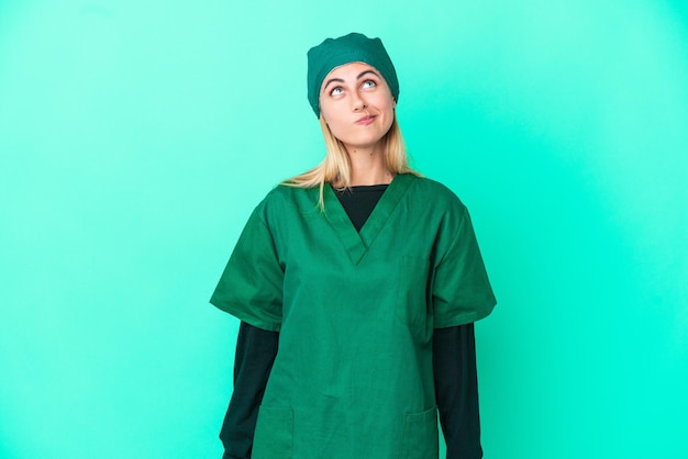 Jovem cirurgiã uruguaia de uniforme verde isolada em fundo azul e olhando para cima