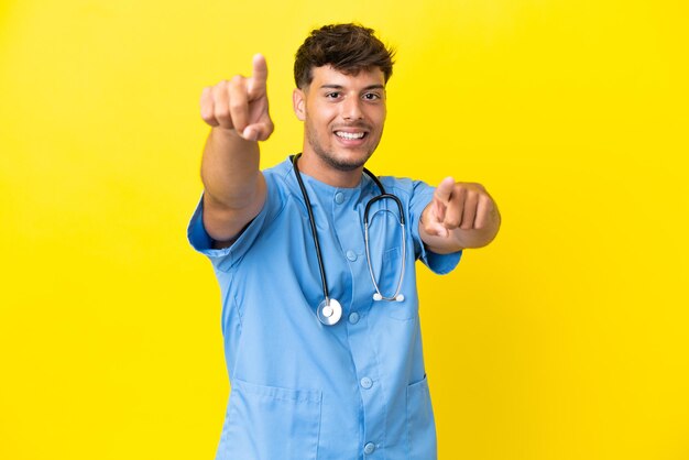 Jovem cirurgião médico isolado em um fundo amarelo apontando o dedo para você enquanto sorri