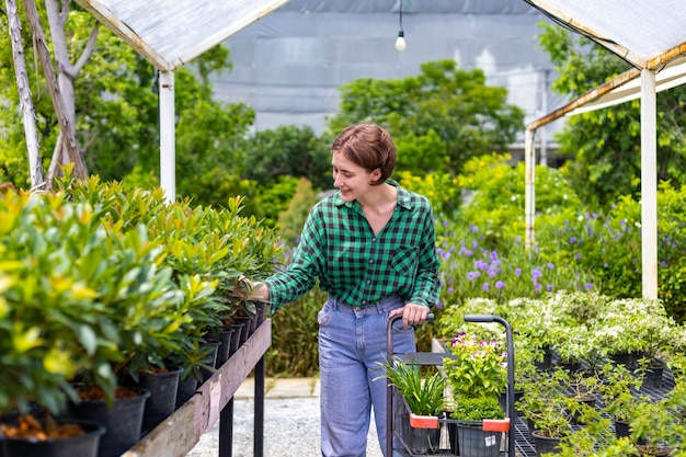Jovem cliente caucasiano está escolhendo planta exótica do viveiro do centro de jardim local com carrinho de compras cheio de planta de verão para jardinagem de fim de semana e conceito ao ar livre