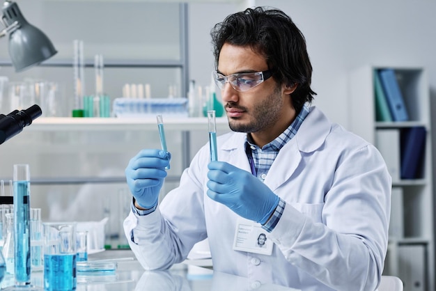 Jovem clínico masculino sério segurando dois frascos com líquido azul em laboratório