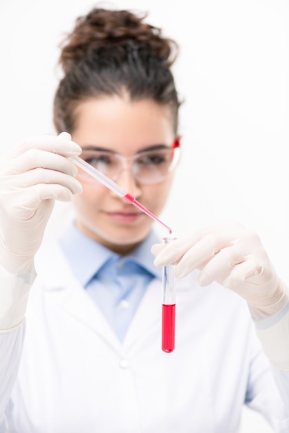 Jovem clínico ou químico em óculos de proteção, luvas e bata branca, adicionando fluido vermelho ao frasco com a nova vacina