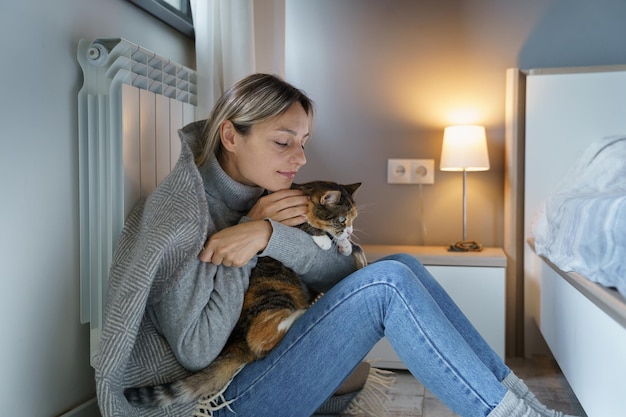 Jovem coberta com cobertor quente gosta de abraçar gato e ficar em casa com animal de estimação favorito