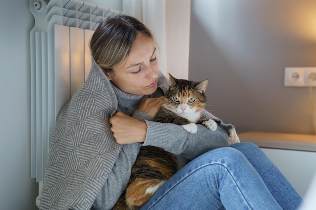 Jovem coberta com cobertor quente se sente melhor abraçando gato doméstico e tenta continuar a vida