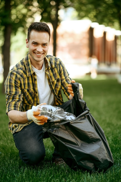 Foto jovem coleta lixo em um saco no parque, voluntário. homem limpa floresta, restauração ecológica, estilo de vida ecológico, coleta e reciclagem de lixo, cuidado ecológico, limpeza ambiental