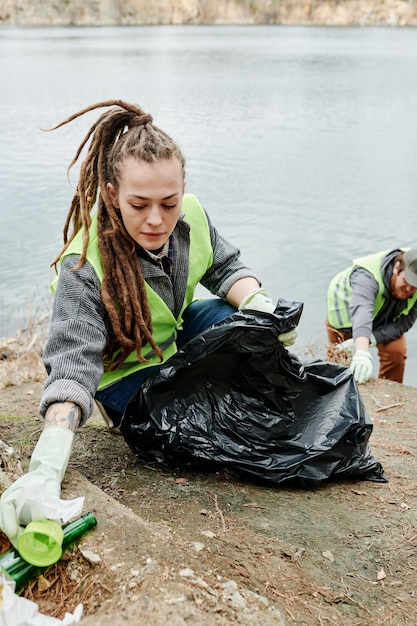 Jovem coletando lixo na beira do lago