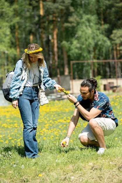 Jovem colhendo dente de leão enquanto faz uma chave de flores para uma namorada no campo