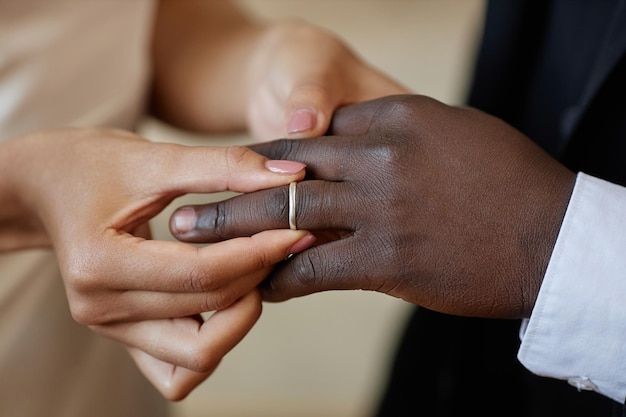 Jovem colocando a aliança no dedo do marido durante a cerimônia de casamento