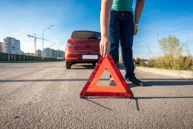 Jovem colocando um triângulo vermelho cantando na estrada após um acidente de carro