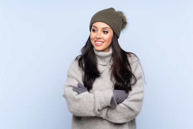 Jovem colombiana com chapéu de inverno sobre parede azul isolada rindo