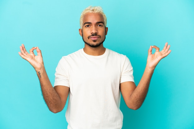 Jovem colombiano bonito isolado em um fundo azul em pose zen