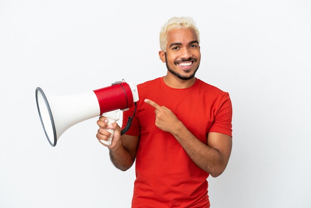 Jovem colombiano bonito isolado no fundo branco segurando um megafone e apontando o lado