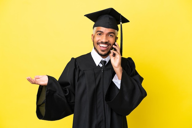 Jovem colombiano graduado pela universidade, isolado em um fundo amarelo, conversando com alguém ao telefone celular