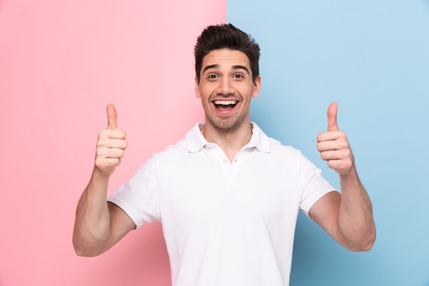 Jovem com a barba por fazer aparecendo os polegares com um sorriso feliz, isolado sobre uma parede colorida