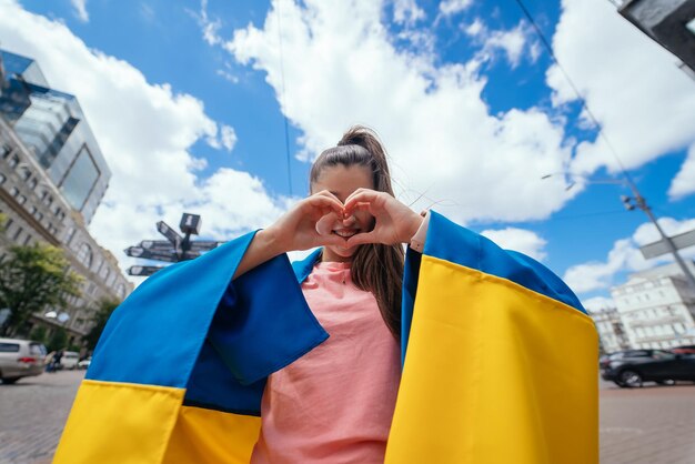 Jovem com bandeira ucraniana mostra coração com as mãos