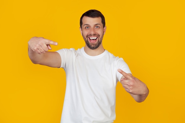 Jovem com barba em uma camiseta branca, apontando com os dedos para a câmera com uma cara feliz e engraçada.