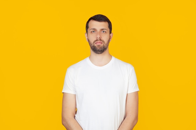 Jovem com barba em uma camiseta branca com uma expressão séria no rosto.