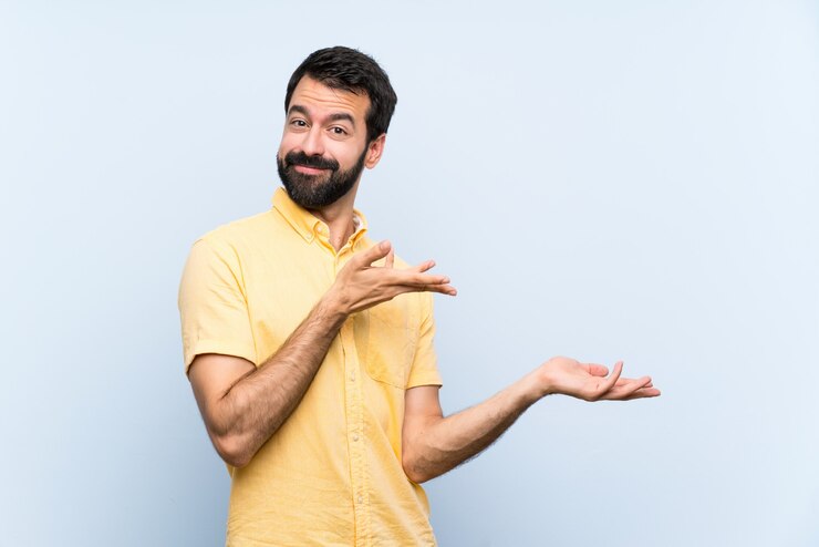 Foto jovem com barba isolado azul, estendendo as mãos para o lado por convidar para vir