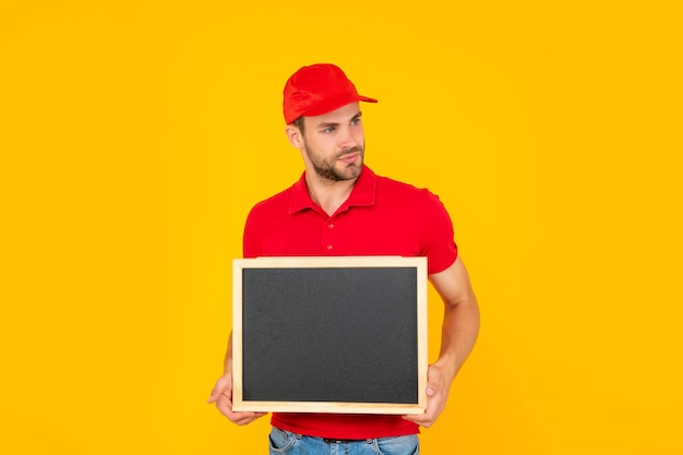 Jovem com barba por fazer de camisa vermelha segurando uma lousa com espaço de cópia em fundo amarelo, anúncio