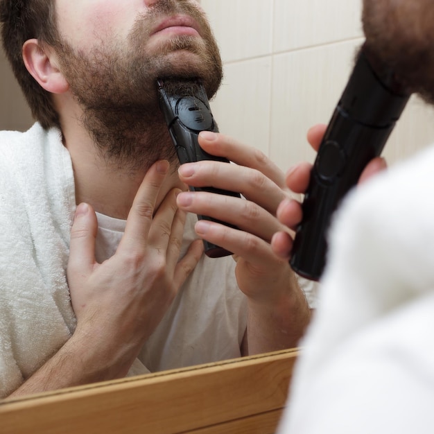 Foto jovem com barba raspar restolho com barbeador elétrico