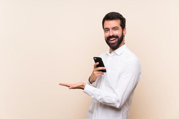 Jovem, com barba, segurando um celular apresentando uma idéia enquanto olha sorrindo para