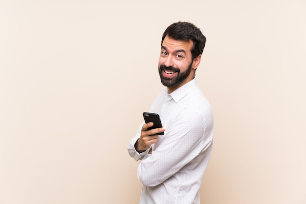 Jovem com barba segurando um celular com os braços cruzados e olhando para a frente