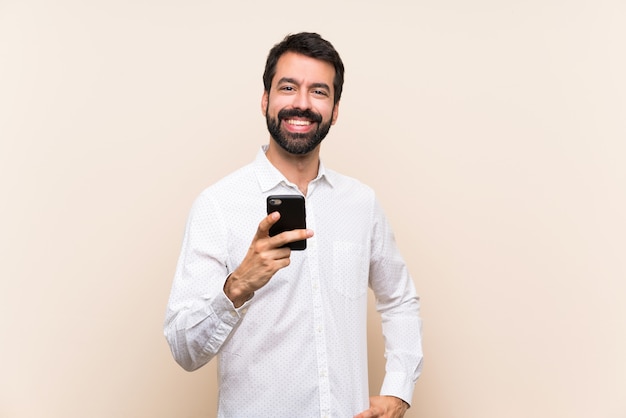 Jovem, com barba, segurando um celular, enviando uma mensagem com o celular