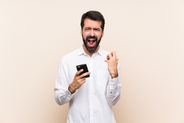 Jovem, com barba, segurando um celular frustrado por uma situação ruim