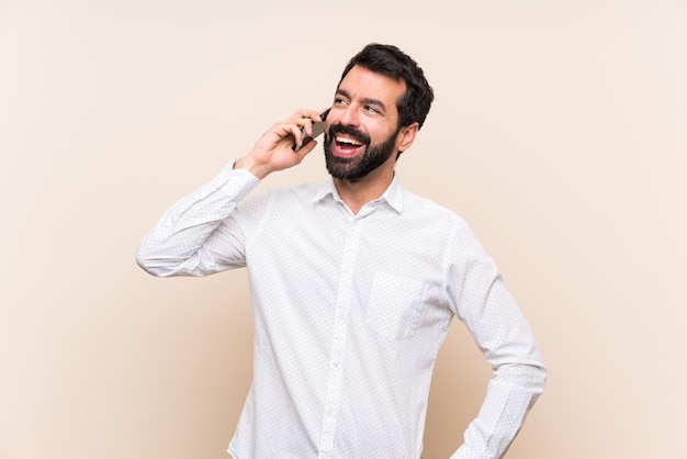 Jovem, com barba, segurando um celular mantendo uma conversa com o telefone móvel