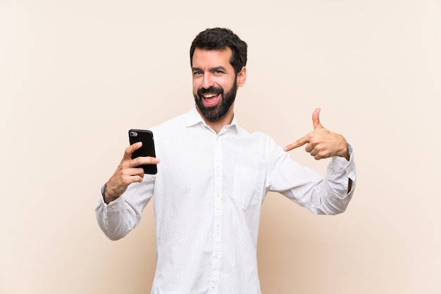 Jovem, com barba, segurando um celular orgulhoso e satisfeito