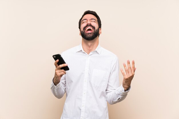 Jovem, com barba, segurando um celular sorrindo muito