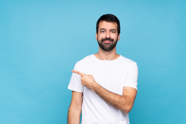 Jovem com barba sobre azul apontando para o lado para apresentar um produto