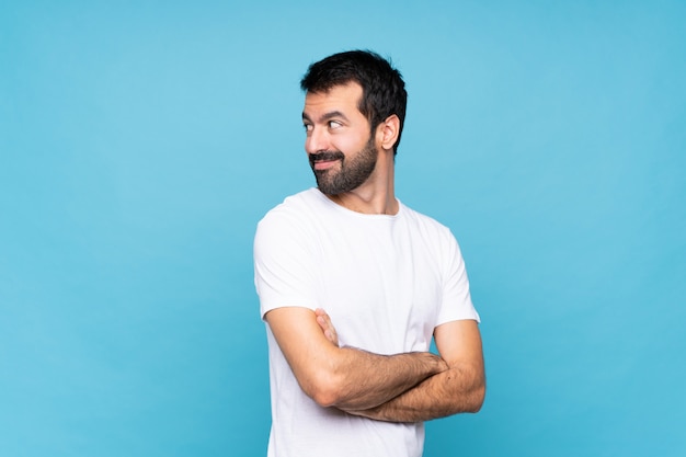 Jovem com barba sobre azul com os braços cruzados e feliz