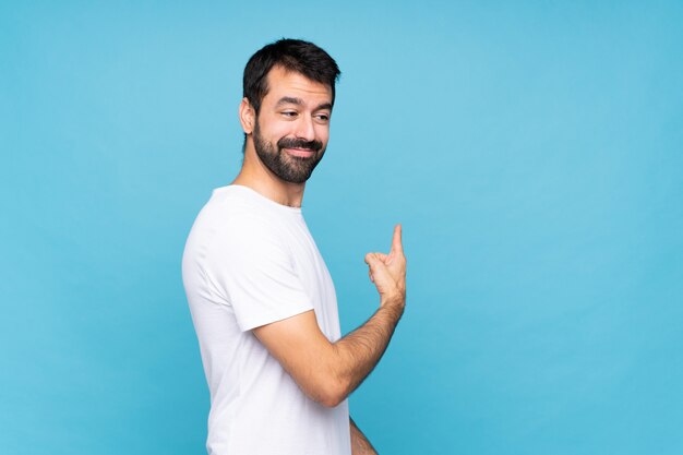 Jovem com barba sobre azul isolado apontando para trás