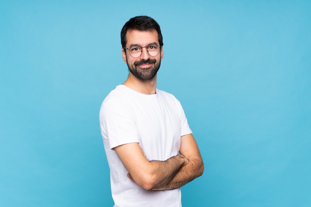 Jovem com barba sobre azul isolado com óculos e sorrindo