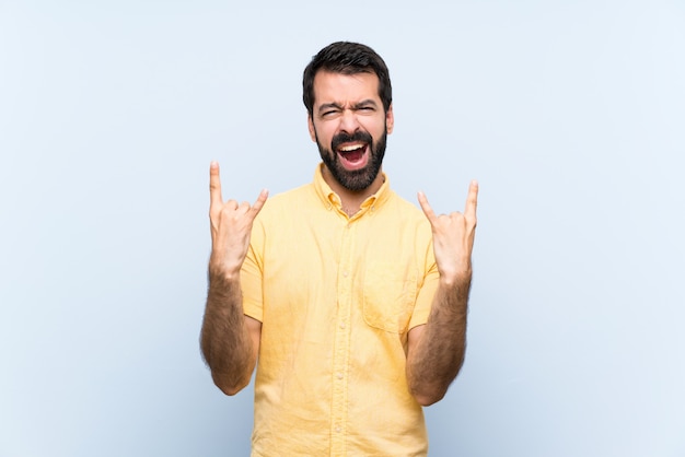 Jovem com barba sobre azul isolado fazendo gesto de pedra