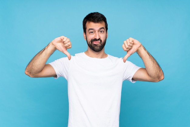 Jovem com barba sobre azul isolado mostrando o polegar para baixo