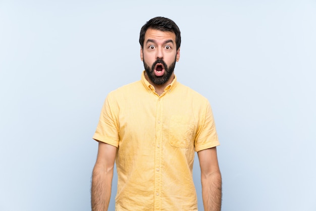 Jovem com barba sobre parede azul isolada com expressão facial de surpresa