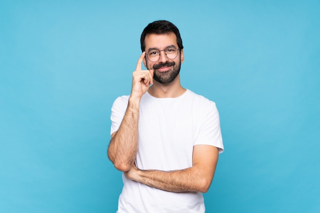 Jovem com barba sobre parede azul isolada com óculos e feliz