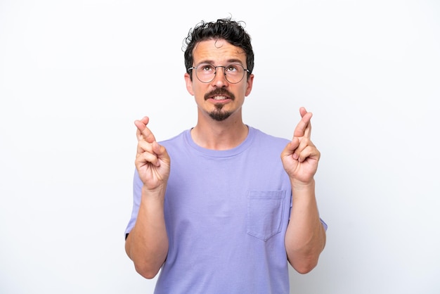 Jovem com bigode isolado em fundo branco com os dedos cruzados e desejando o melhor