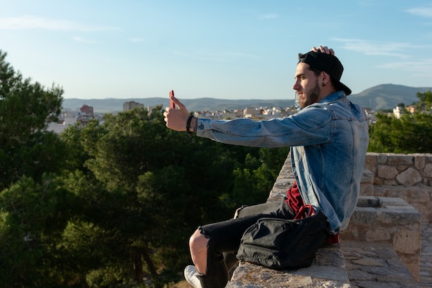 Jovem com boné tira uma foto com a cidade em segundo plano.