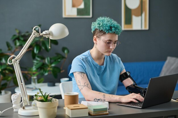 Jovem com braço protético digitando no laptop fazendo seu trabalho online em casa