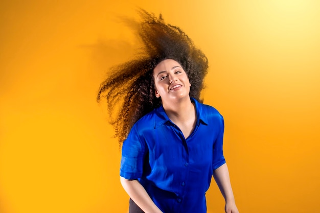 Jovem com cabelo afro balançando o cabelo grande sorrindo em fundo laranja