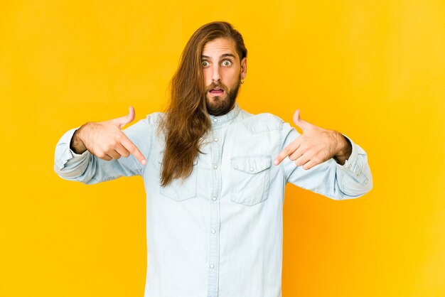 Jovem com cabelo comprido olha aponta para baixo com os dedos, sentimento positivo.