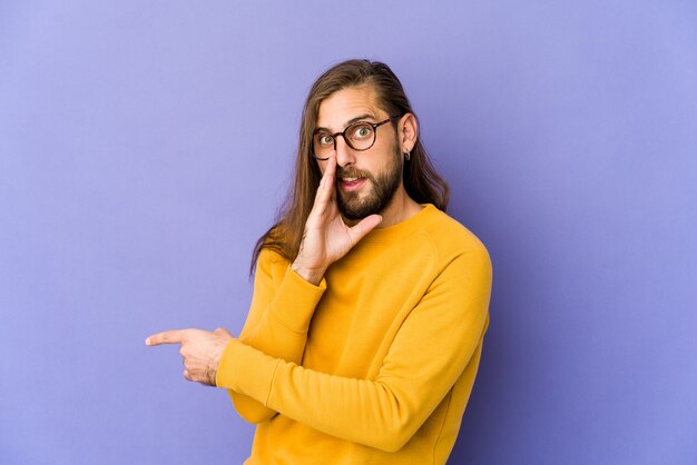 Jovem com cabelo comprido olha dizendo uma fofoca, apontando para o lado relatando algo.