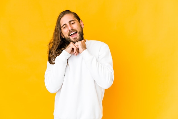 Jovem com cabelo comprido parece manter as mãos embaixo do queixo, olhando feliz para o lado