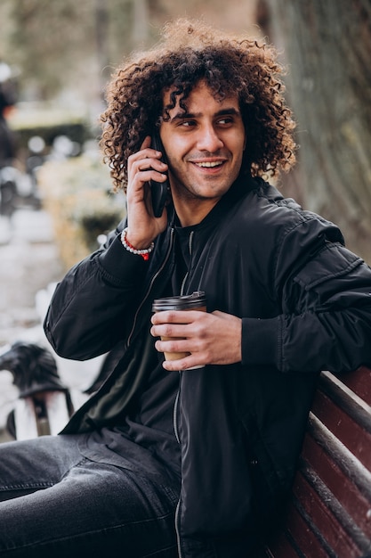 Jovem com cabelo encaracolado tomando café e falando ao telefone