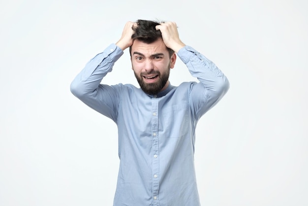 Jovem com cabelo escuro e barba usa camisa azul parece lábios zangados franzidos sobrancelhas franzidas