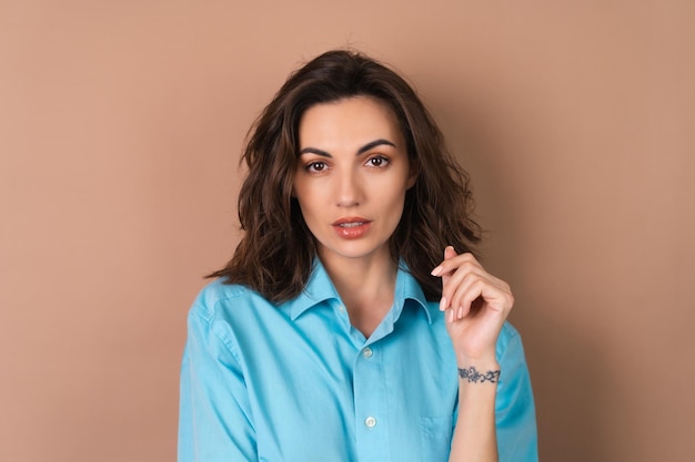 Jovem com cabelo volumoso ondulado e maquiagem natural diurna vestindo uma camisa azul sobre fundo bege