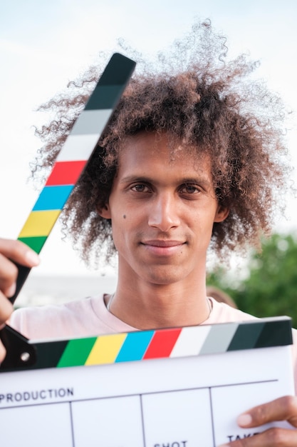 Jovem com cabelos encaracolados ativando um clapperboard de filme para começar uma gravação conceito de estilo de vida