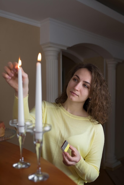 Jovem com cabelos longos acende velas na cozinha em casa